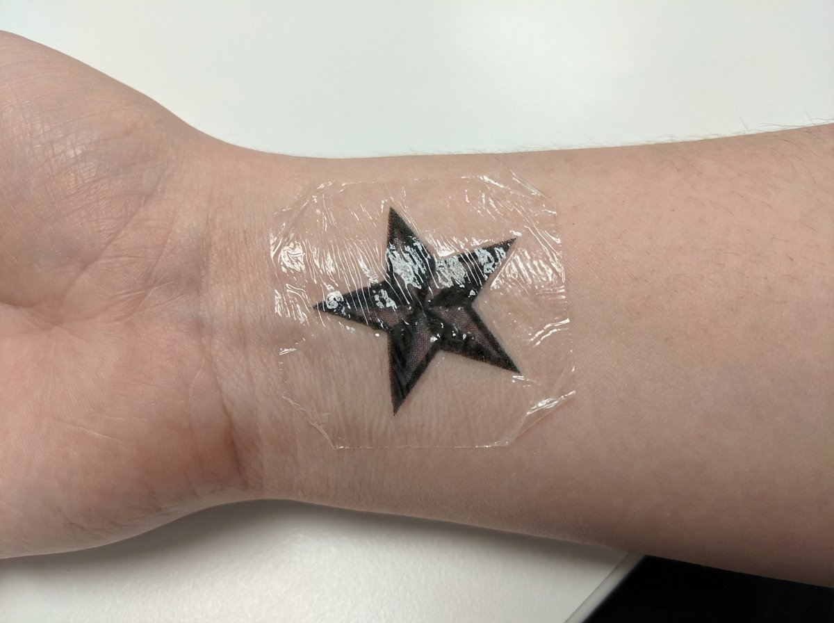 Water-transfer temporary tattoo with visible shiny film peeling at edges